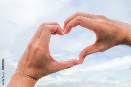 Hand in heart sign on sky background
