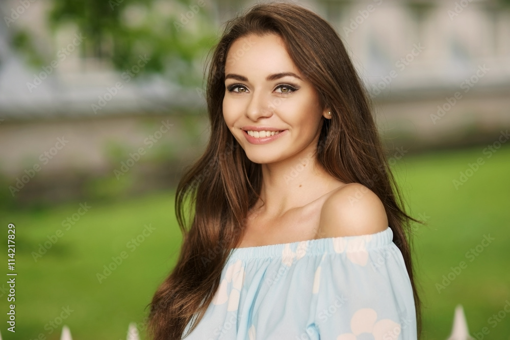 Fototapeta premium Young beautiful woman with long brunette hair and perfect smile. Happy girl posing in park and looking in camera