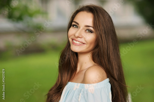 Young beautiful woman with long brunette hair and perfect smile. Happy girl posing in park and looking in camera photo