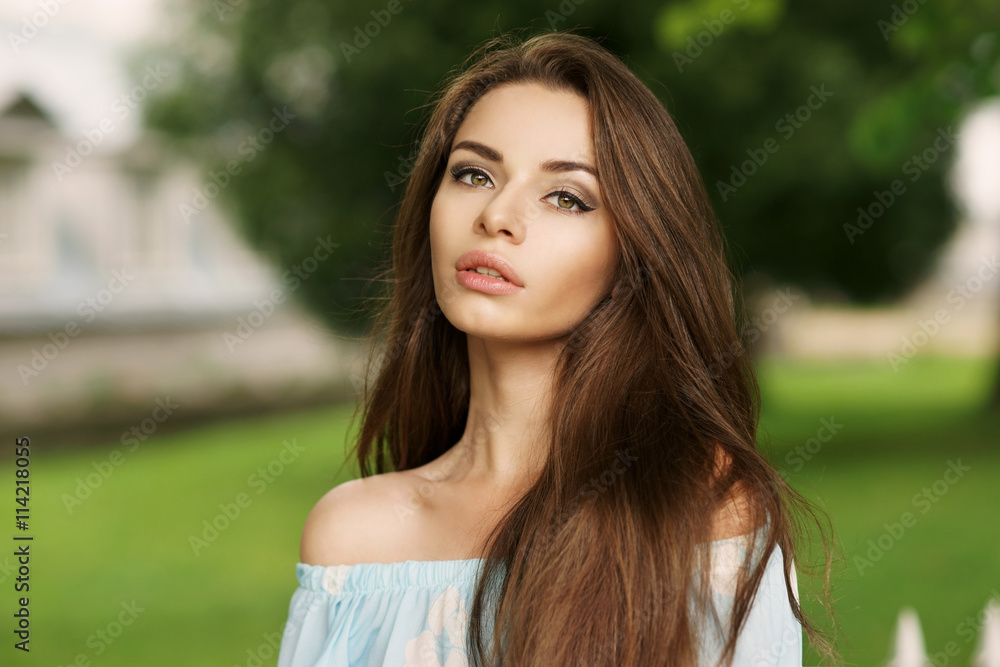Young beautiful woman with long brunette hair. Calm girl with perfect clean skin posing in park and looking in camera Young beautiful woman with long brunette hair. Calm girl with perfect clean skin posing in park and looking in camera