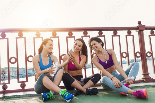 Three sportive pretty women taking a break while out for a run - on city bridge at sunset