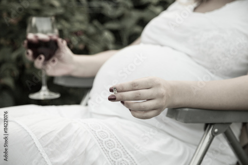Young pregnant woman holding wine and cigarette