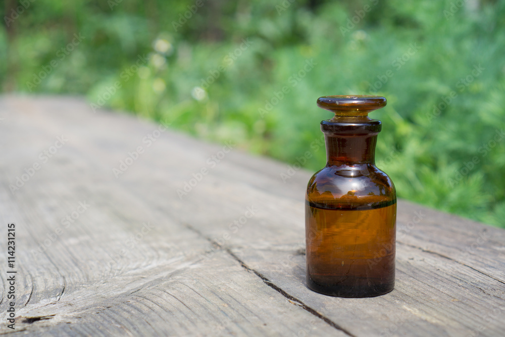 Little brown bottle with water or liquid on wooden board, against the background of vegetation.