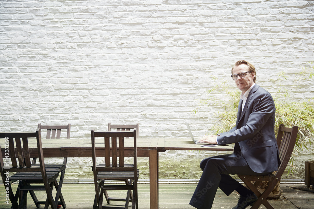 Businessman sitting at table in a backyard working with laptop Businessman sitting at table in a backyard working with laptop