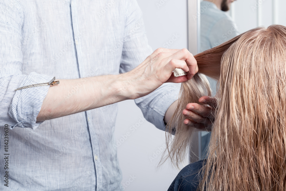 A hairdresser making haircut for a blonde female client in hairdressing salon. Selective focus A hairdresser making haircut for a blonde female client in hairdressing salon. Selective focus
