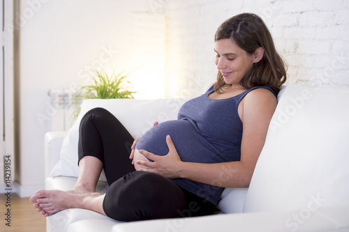 Free Download young beautiful happy 8 or 9 months pregnant woman at home living room couch holding big belly - GFXLoad