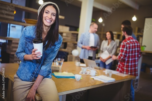 Happy businesswoman holding disposable cup in office