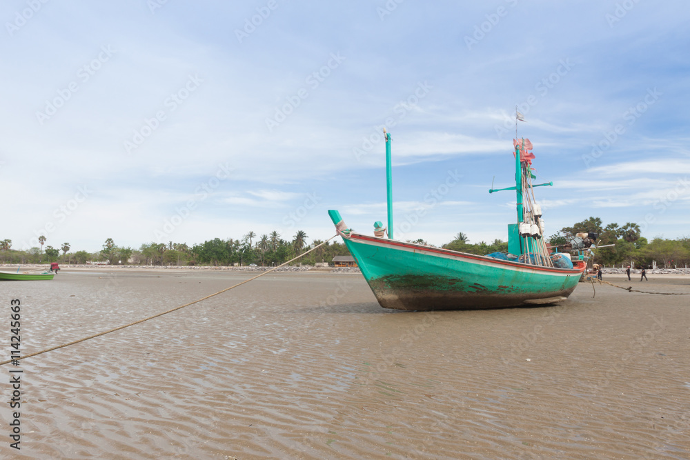Green wooden fishing boat on the  low tide beach.