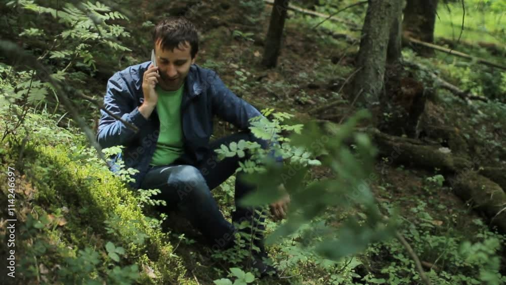 The man in the forest call by smartphone. It sits on a small cliff green The man in the forest call by smartphone. It sits on a small cliff green