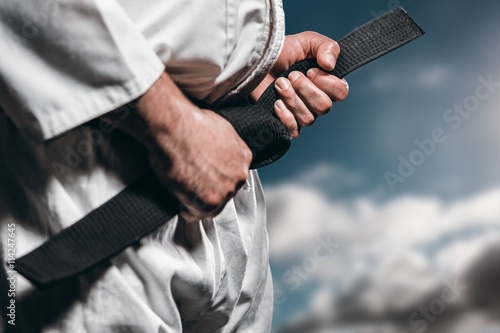 Composite image of fighter tightening karate belt photo