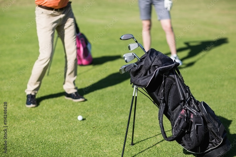 Couple playing golf with bag on foreground Couple playing golf with bag on foreground