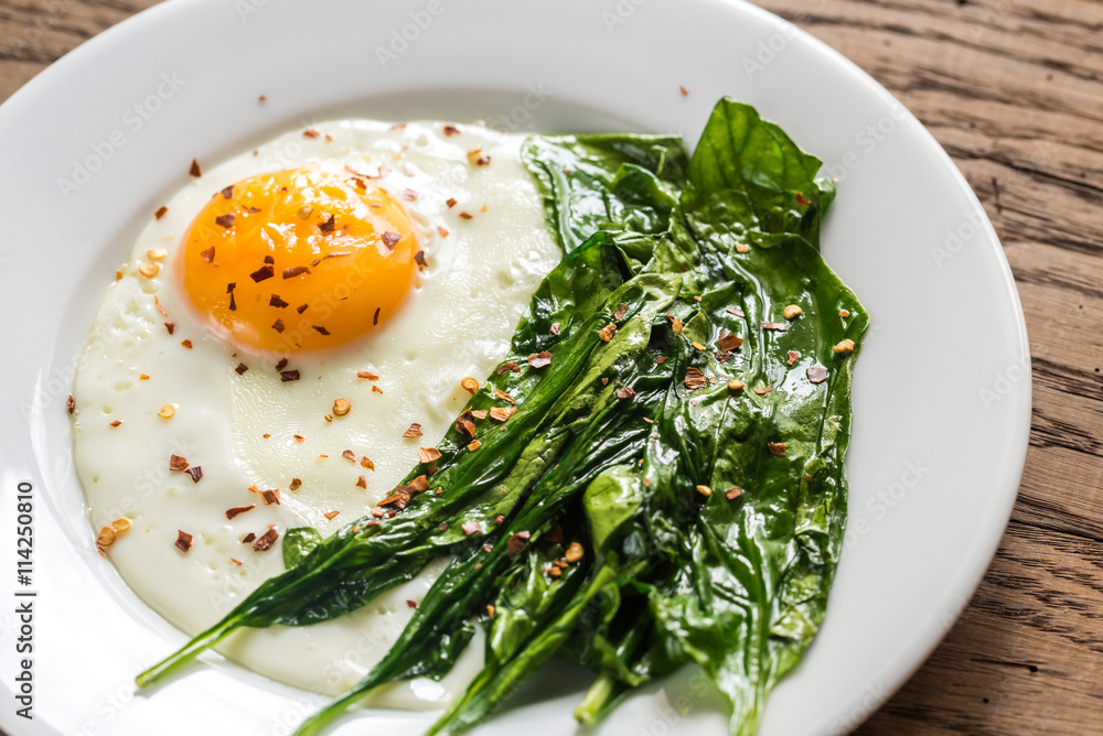 Fried egg with spinach on the wooden table Fried egg with spinach on the wooden table