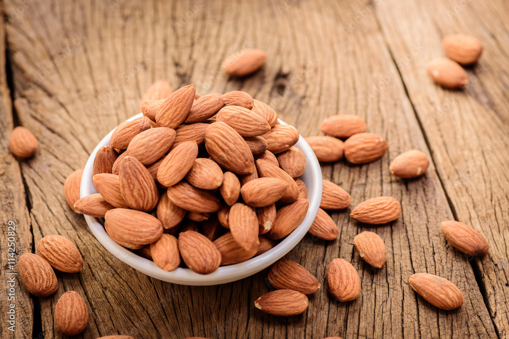 almonds in a white ceramic bowl on grained wood background almonds in a white ceramic bowl on grained wood background
