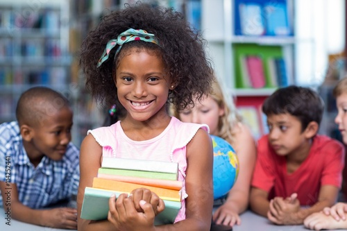 Smiling girl holding books against classmates