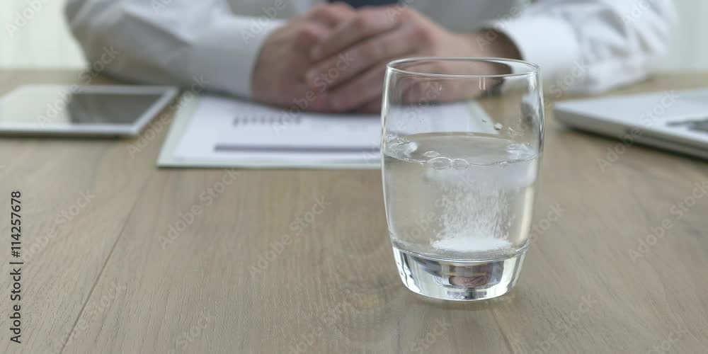 Businessman dropping an effervescent tablet into a glass of water, drugs and healthcare concept Businessman dropping an effervescent tablet into a glass of water, drugs and healthcare concept