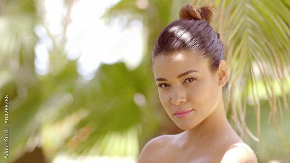 Single beautiful young woman with bare shoulders near large tropical palm tree leaves with copy space for spa concept