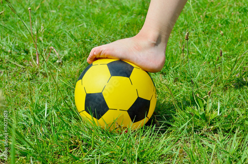 Children s shoeless foot and a soccer ball on green grass.