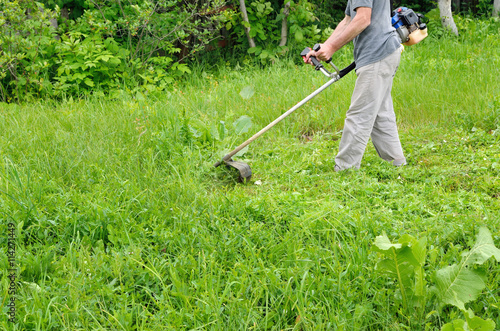 Man mowing lawn mower green, young grass. Gardener doing seasonal work. Clearing the garden of weeds.
