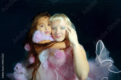 Woman and girl, underwater models, presenting fashion in pool photo