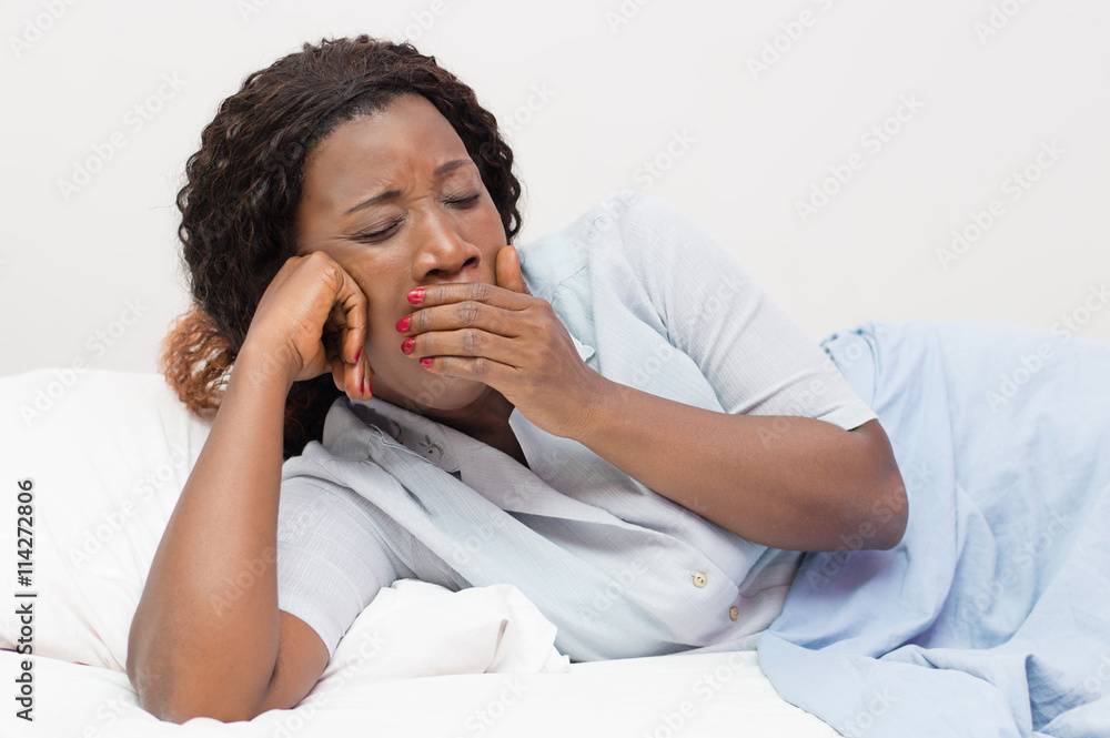 young African woman yawns lying in bed at home young African woman yawns lying in bed at home