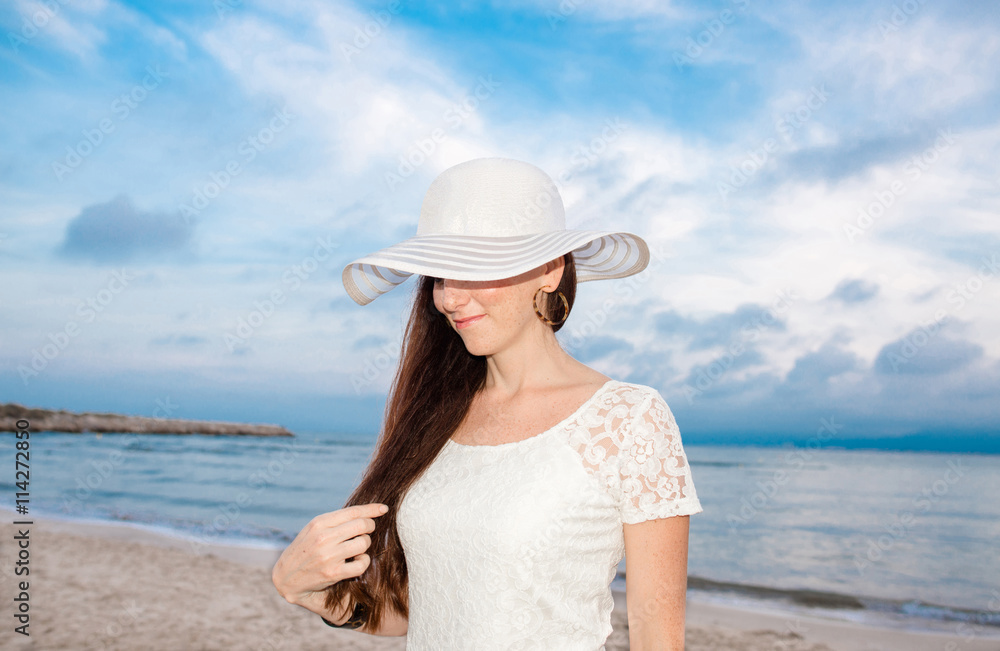 Pretty woman with white hat on the beach. Beautiful young woman with long hair on summer holidays. 