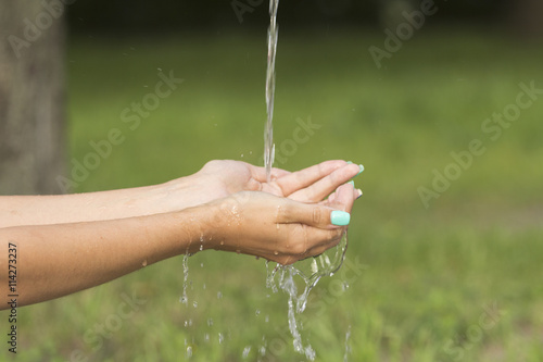 A stream of fresh clean water flowing to the hands of a girl with beautiful manicure