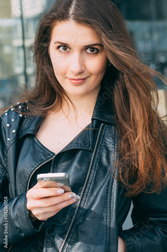 Young woman in leather jacket, outdoor holding a phone 