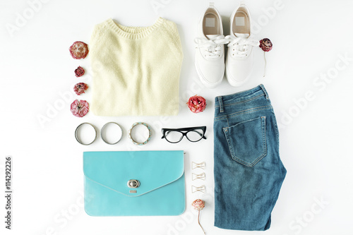 flat lay feminini clothes and accessories collage with cardigan, jeans, glasses, bracelet, clutch, shoes and dry roses on white background.