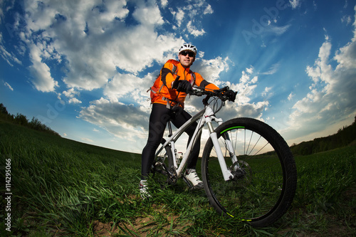 Young man riding on bicycle through deep grass with backpack