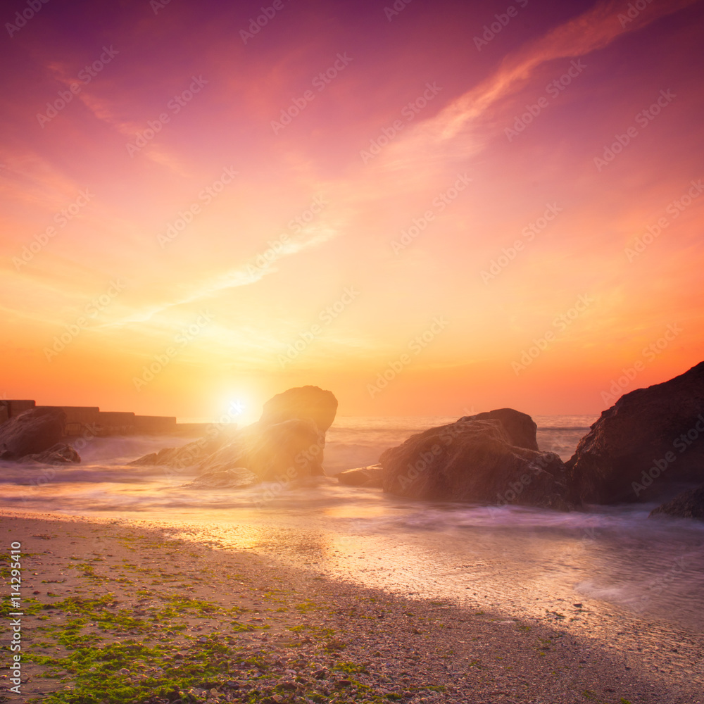 Summer seasonal natural vacation background. Romantic morning at sea. Big boulders sticking out from smooth wavy sea. Pink horizon with first hot sun rays. Long exposure. 