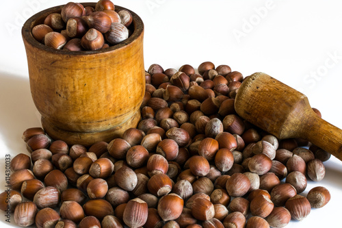 Heap of hazelnuts in a wooden mortar with a wooden pestle on a white background