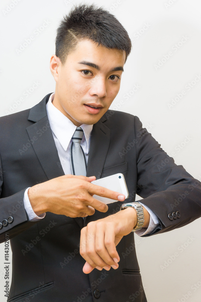 Young asian business man looking at watch and talking on cellpho Young asian business man looking at watch and talking on cellpho