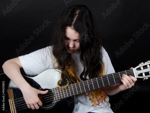 Teenage girl with painted hair playing a black guitar (on a black background)