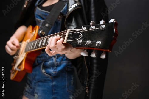 Close up of girl's hands on guitar over black background.