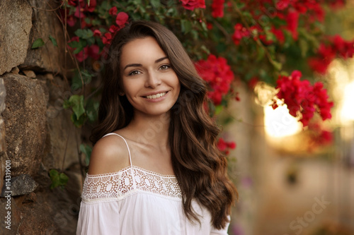 Closeup beauty portrait of young pretty happy smiling girl with dark curly hair looking at you. Soft sunset backligth photo