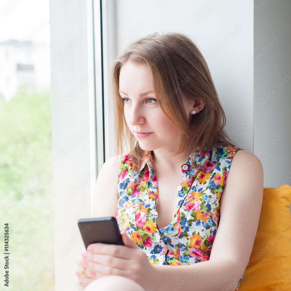 young beautiful girl sitting on the window with the phone young beautiful girl sitting on the window with the phone
