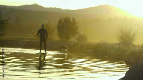 Man in wetsuit paddleboards in golden sunset on Deschutes River in Bend, Oregon photo