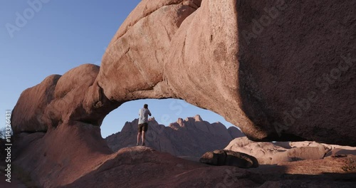 4K male tourist entering into the famous arch of the Spitzkoppe mountains and taking a picture photo