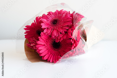 Fotografi Front on view of crimson gerberas wrapped in brown paper and cellophane lying on
