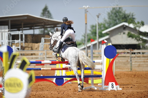 The rear view on the rider overcomes the obstacle on the horse jumping competition