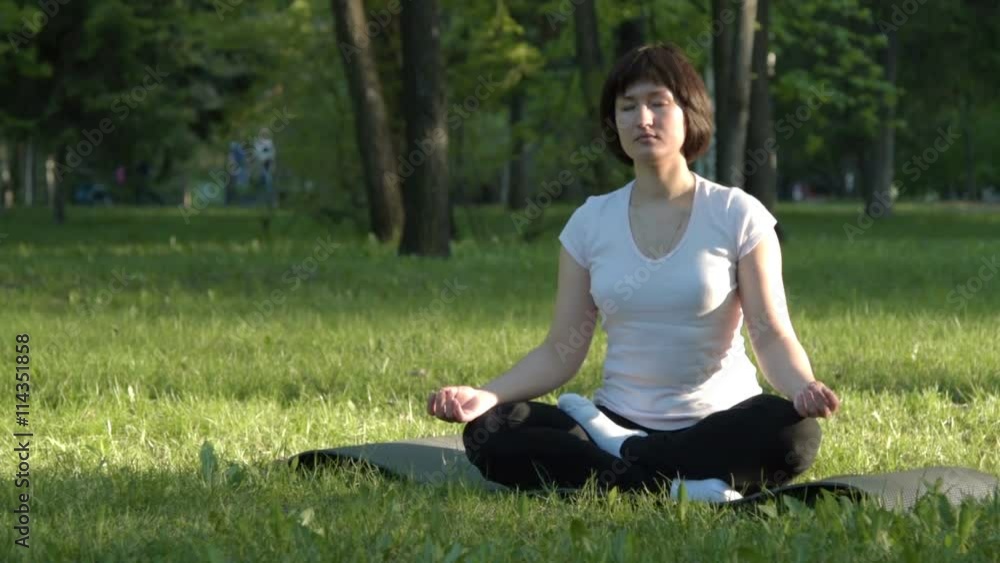 Young woman meditating in lotus pose in green park at sunset Young woman meditating in lotus pose in green park at sunset