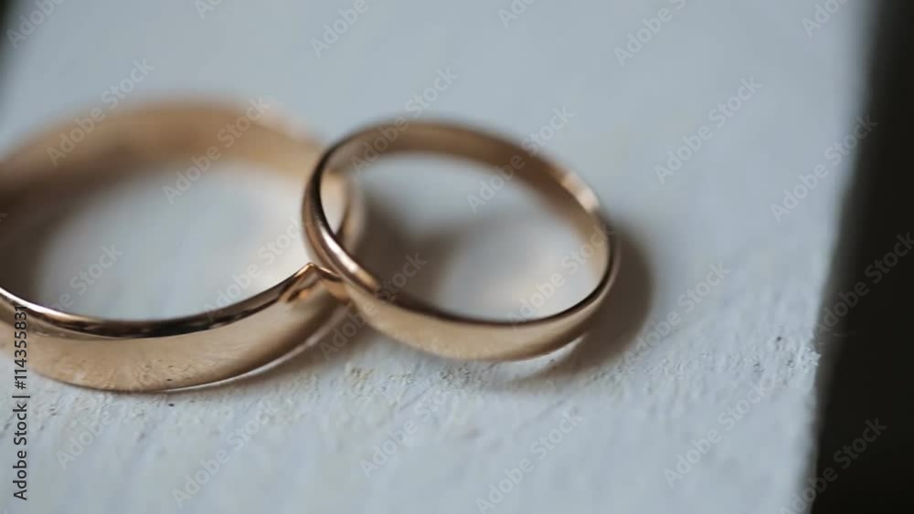 Two golden rings lie on wooden table painted in white color. Two golden rings lie on wooden table painted in white color.