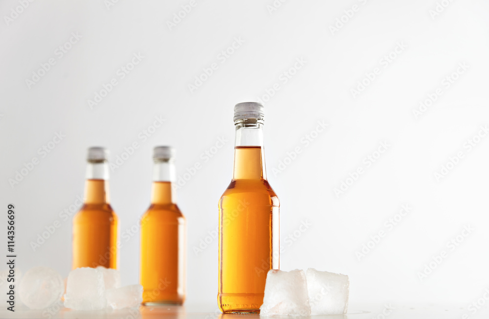 Three sealed bottles with cold cider drink inside isolated on white between ice cubes, presentation mockup Three sealed bottles with cold cider drink inside isolated on white between ice cubes, presentation mockup