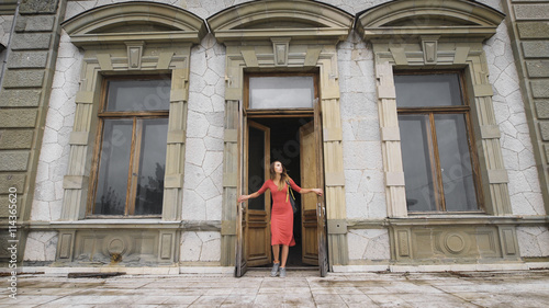 Attractive girl in red dress goes on the balcony of an old manor. © kustvideo