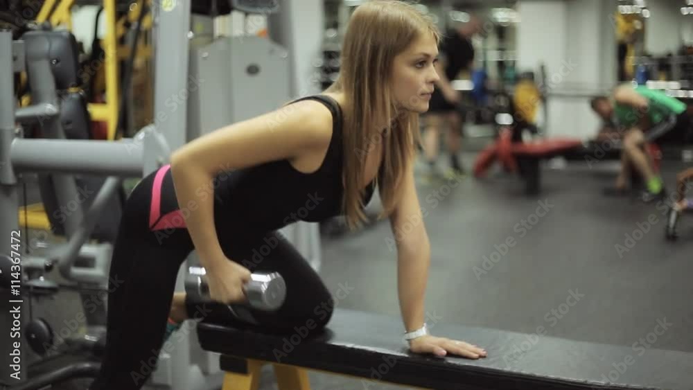 Woman in gym lifting dumbbell at bench. Woman in gym lifting dumbbell at bench.