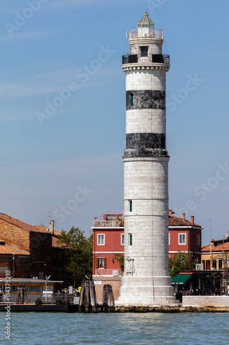 Faro di Murano Lighthouse on the Venetian island of Murano, a round cylindrical stone tower with three black horizontal bars near the top, built in 1912.