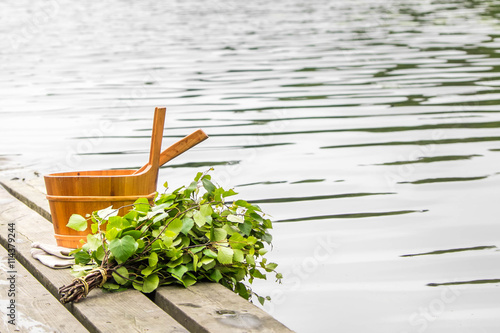Sauna whisk and wooden bucket next to lake