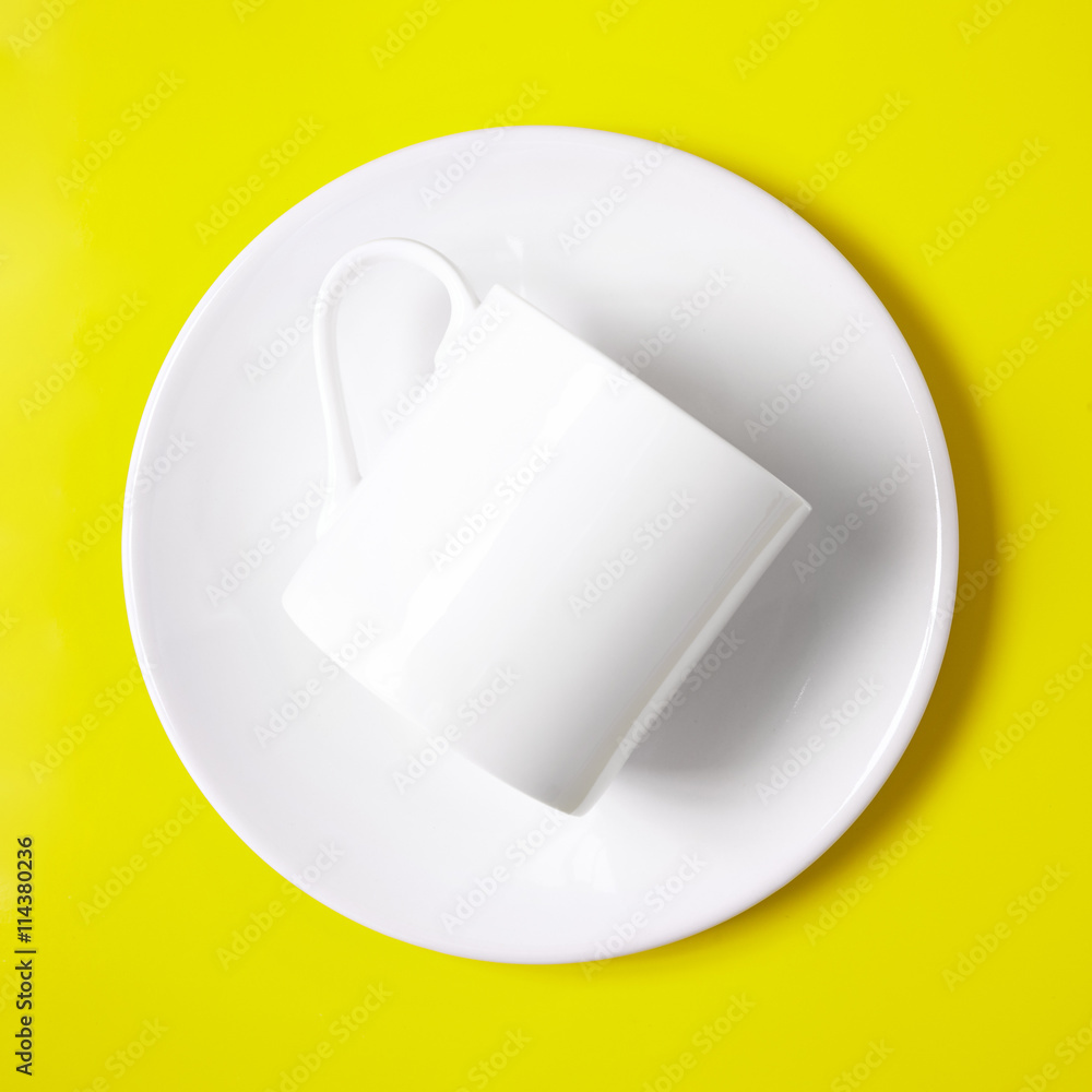 Crockery, plates, mugs and dishes - a plain white coffee cup and saucer on a yellow background Crockery, plates, mugs and dishes - a plain white coffee cup and saucer on a yellow background