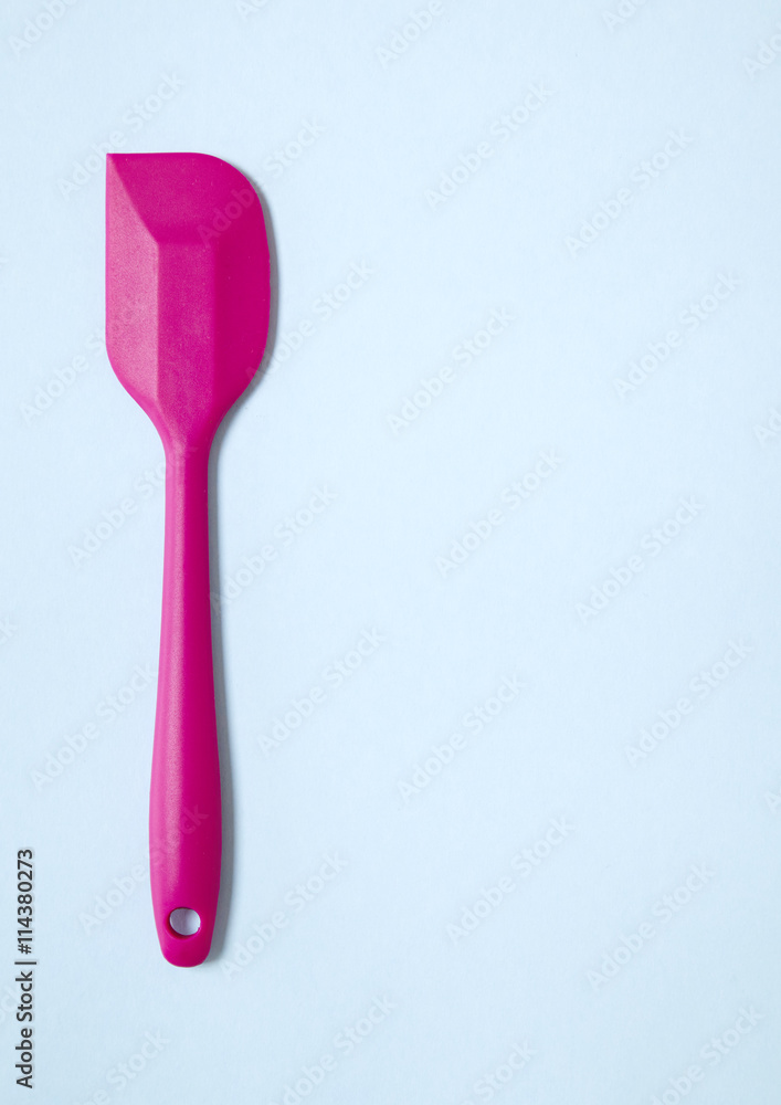Cooking utensils - a pink silicone baking spatula on a blue background forming a page border Cooking utensils - a pink silicone baking spatula on a blue background forming a page border