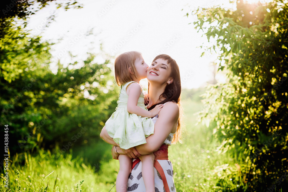 Mom kisses and hugs daughter on nature in sunset light, family, motherhood, child Mom kisses and hugs daughter on nature in sunset light, family, motherhood, child